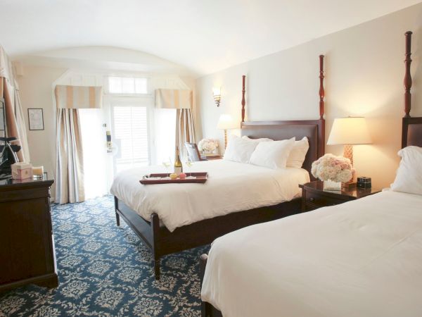 A bright hotel room with two neatly made beds, floral decor, lamps, and a patterned blue carpet.