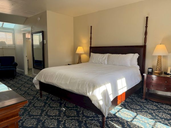 A hotel-style bedroom with a large bed, two lamps, and a nightstand beside a sliding glass door.