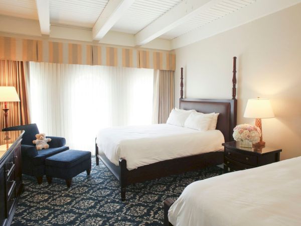 A tidy hotel bedroom with a large bed, bedside lamps, curtains, and an armchair by the window.