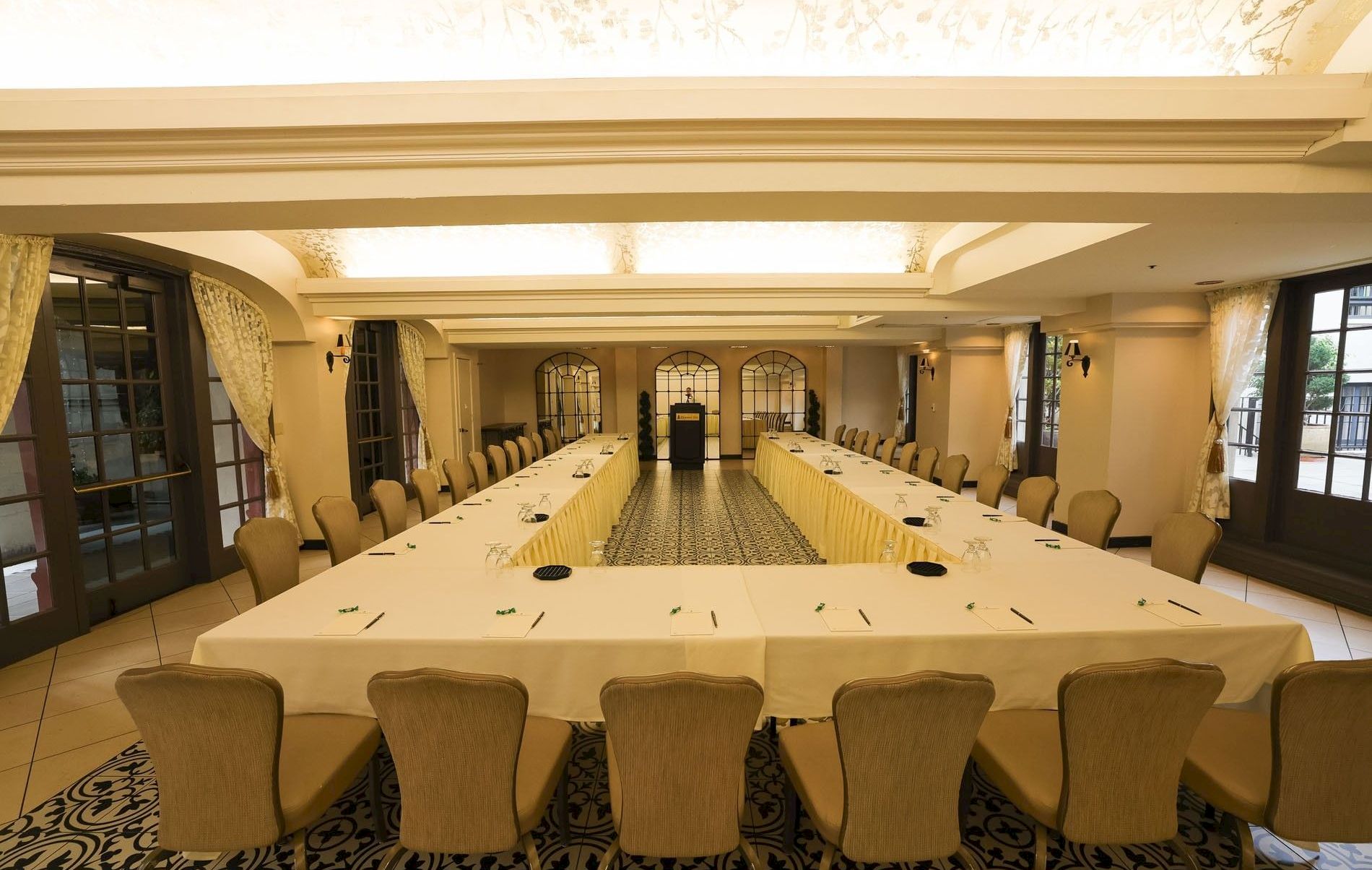 A formal conference room with long tables set for a meeting, chairs around them, and decorative arches at the far end.