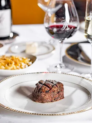 A fine-dining table set with steak bites and sides, plus glasses of red and white wine.