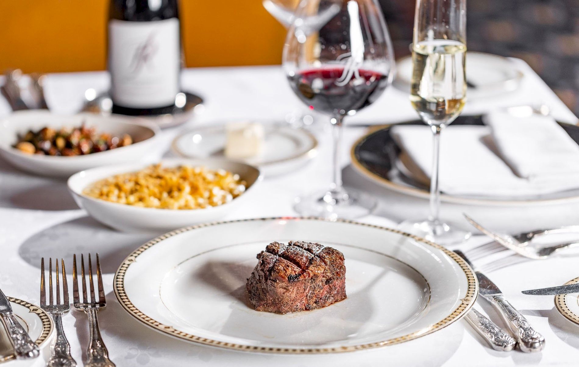 A fancy dining table with steak, pasta, and glasses of red and white wine.