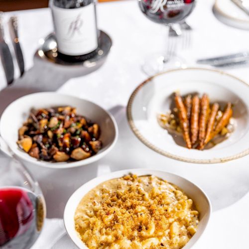 A plated meal spread on a table with bowls of food and two wine glasses, ready for dining.