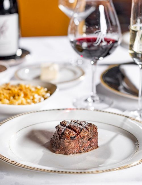 A fancy dinner table set with steak, sides, and sparkling wine glasses for a restaurant meal.