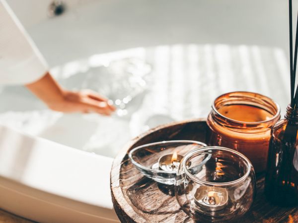 A spa setup with essential oil bottles, candles on a wooden tray, and a blurred hand holding a towel.