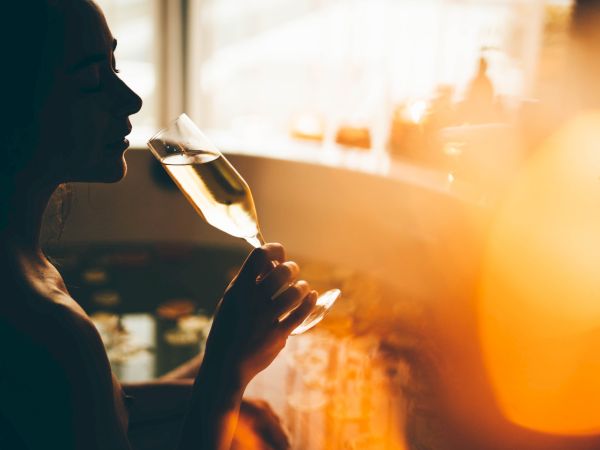 A person&rsquo;s profile holds a wine glass at sunset, silhouetted against a warm, glowing window view.