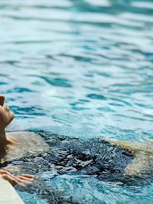 A person’s head is above the water in a swimming pool, gazing toward the rippling surface.