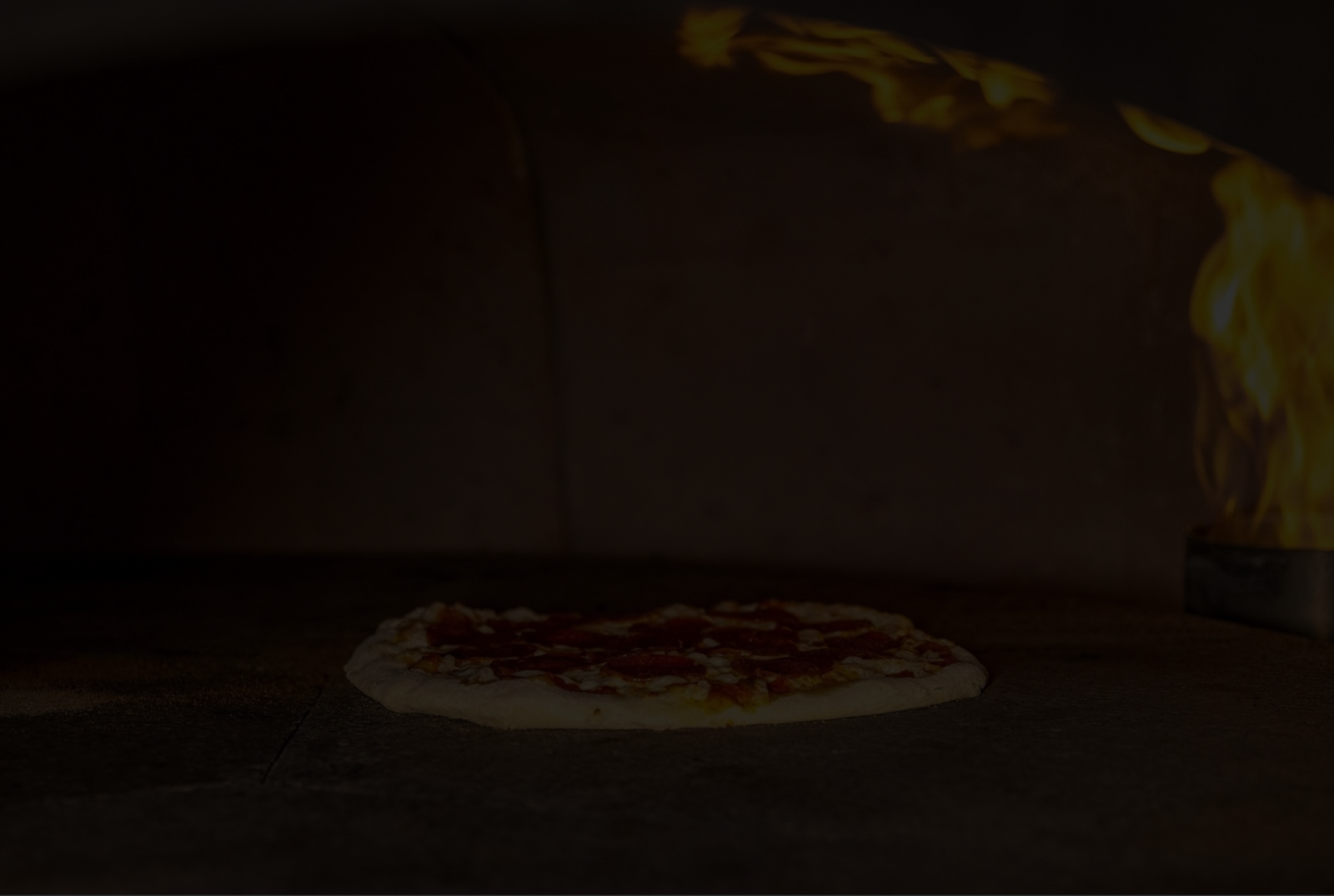 A pepperoni pizza lies on the floor as a hand throws toppings in the dark background.