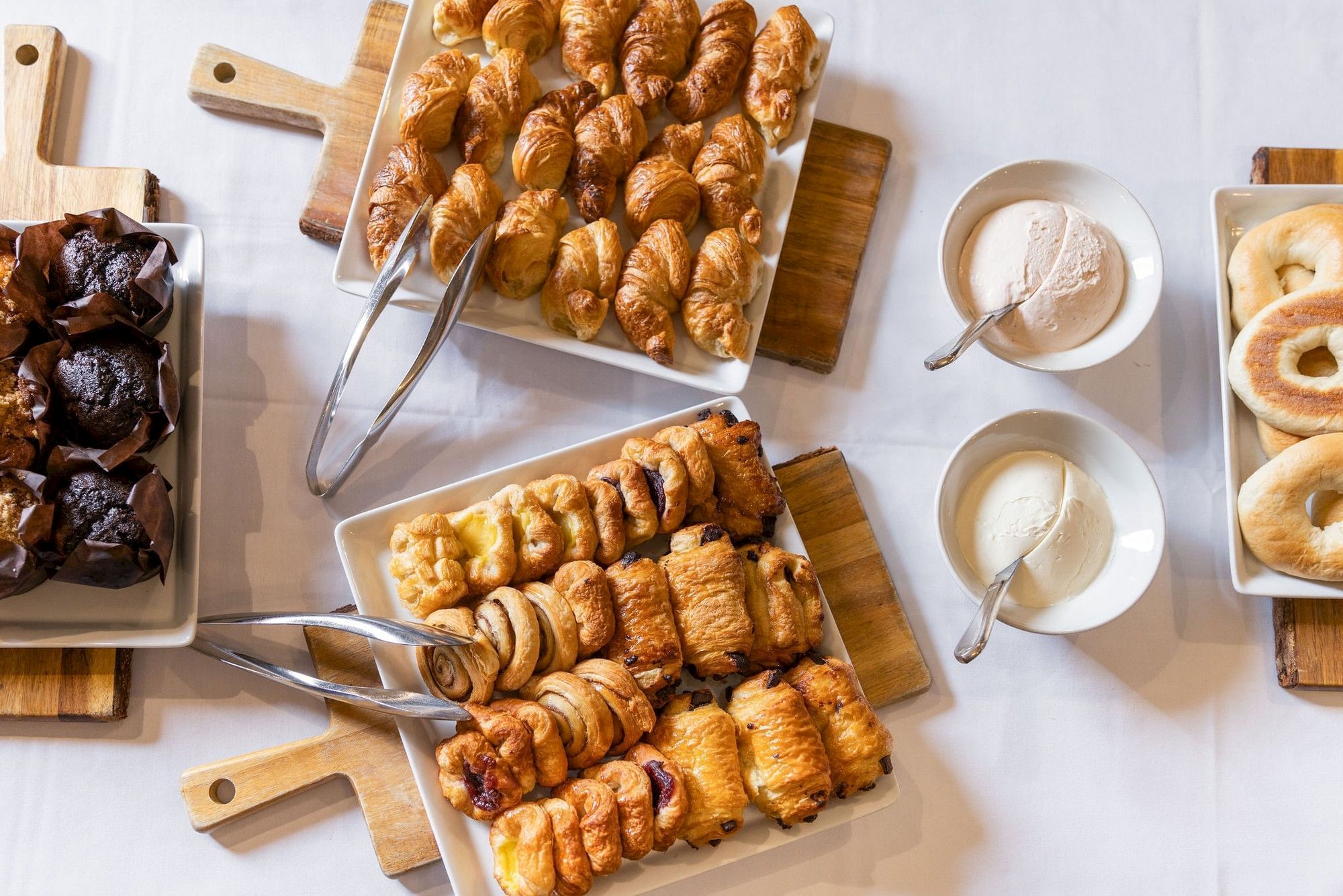 Assorted baked pastries&mdash;croissants and rolls&mdash;on trays with bowls of white cream/dip for serving.