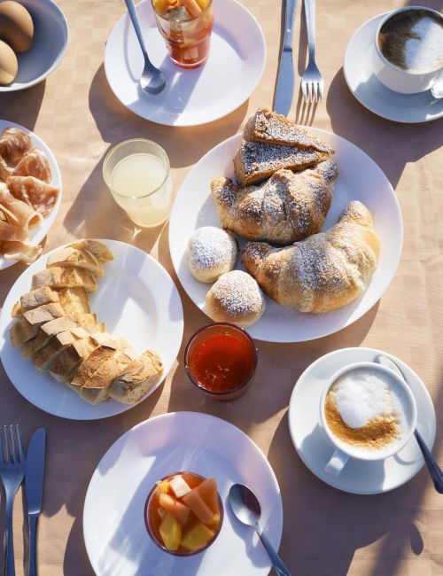 Breakfast/brunch spread with pastries, fruit, juice, coffee, and jam on plates.