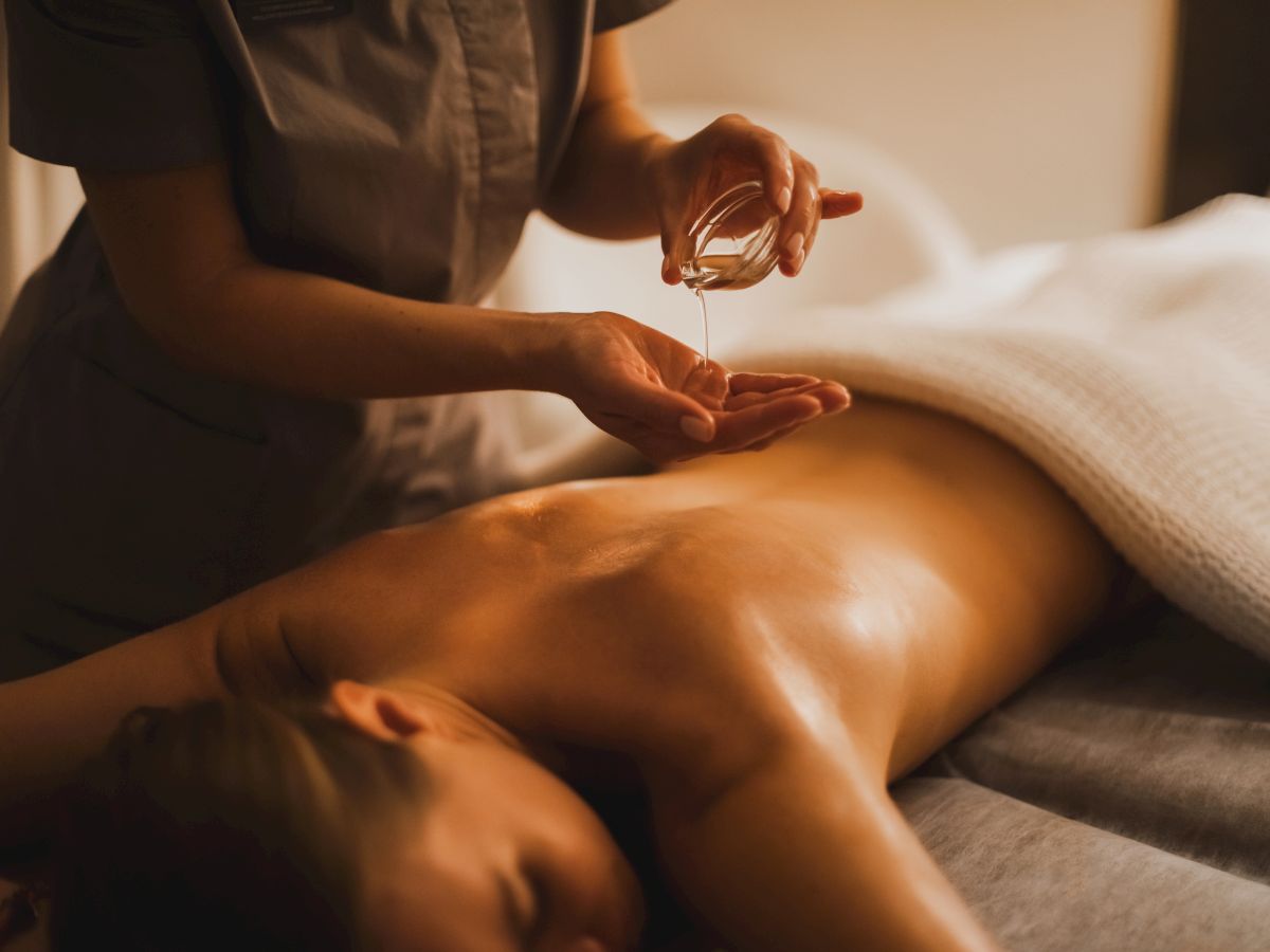 A therapist pours massage oil into their hands and applies it to a person&rsquo;s bare back in a relaxing massage.