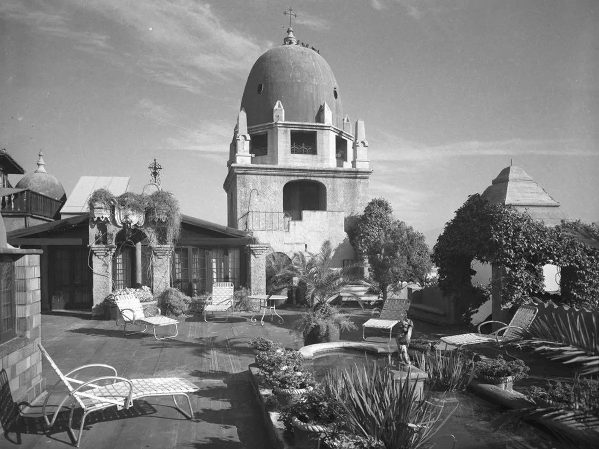 Black-and-white courtyard with lounge chairs and a large dome-topped building under a cloudy sky.